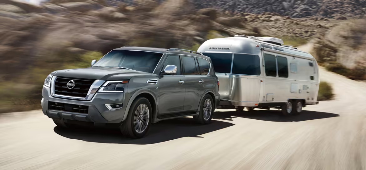 Nissan Armada 2024 gris tirant une roulotte sur une route de terre en région désertique.
