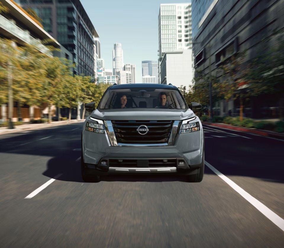 Nissan Pathfinder gris vu de face en conduite urbaine sur une rue bordée de gratte-ciel modernes.