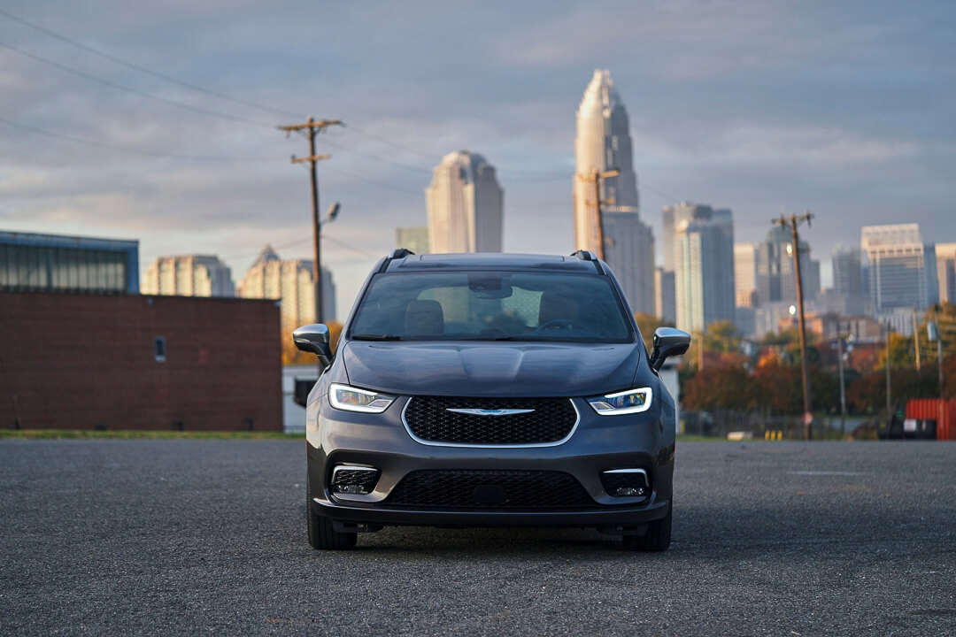 Chrysler Pacifica hybride 2022 stationnée face à la caméra avec les gratte-ciel en arrière-plan au lever du jour.