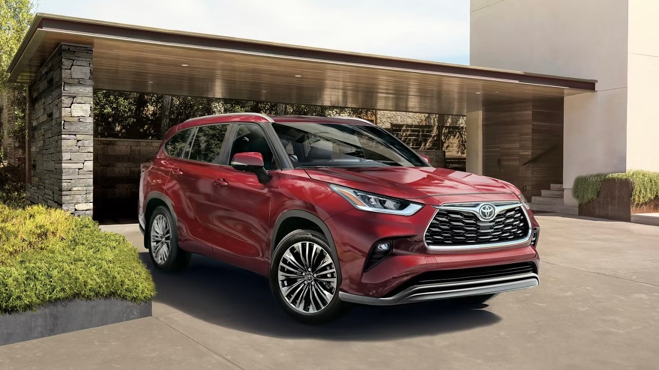 Toyota Highlander Hybride 2025 rouge stationné devant une maison moderne avec entrée en béton et végétation.