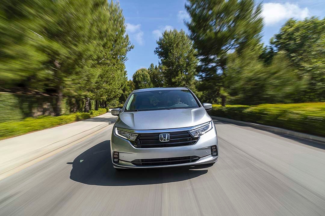 Honda Odyssey 2022 argent vue de face sur une route bordée d’arbres par une journée ensoleillée.